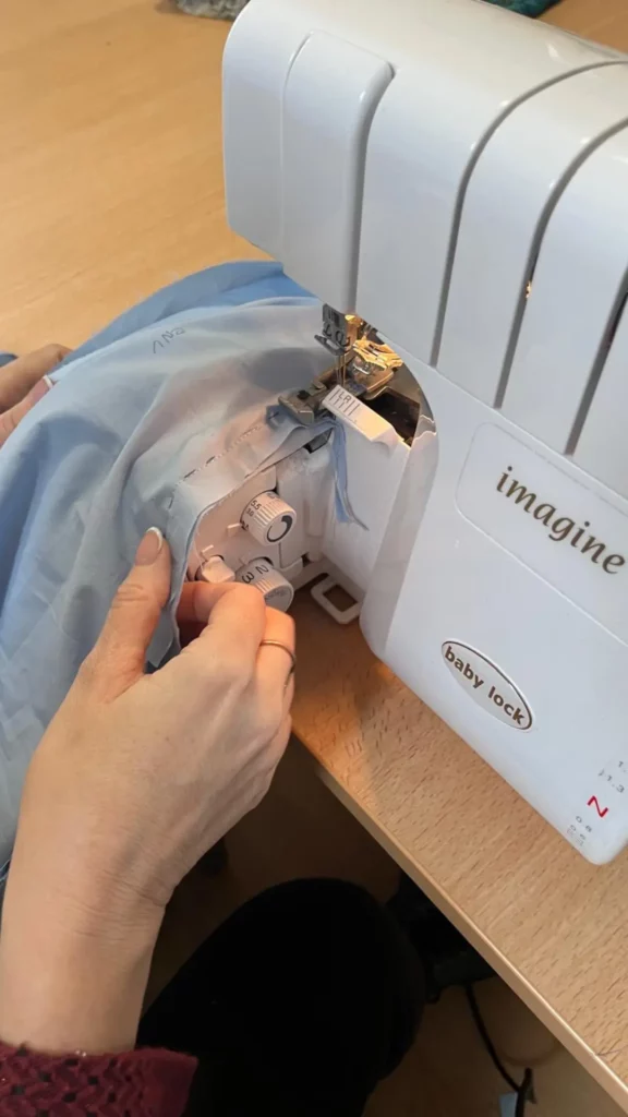 Gros plan d’une machine à coudre surjeteuse Baby Lock en cours d’utilisation pour assembler un tissu bleu lors d’une formation couture.