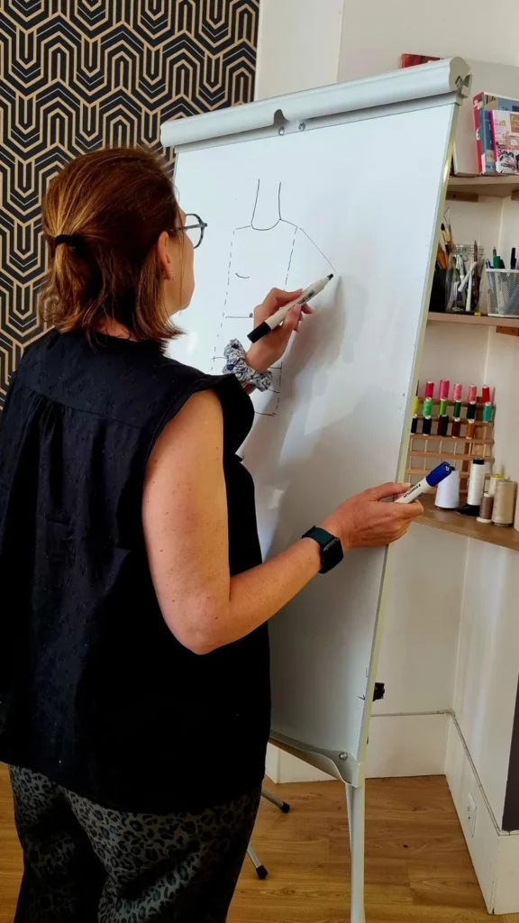 Personne en formation de couture dessinant un patron de vêtement sur un tableau blanc lors d’un cours pratique.